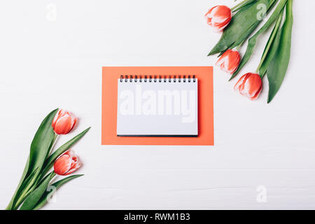 Flach Anordnung der offenen leere Notepad auf rotem Papier Blatt in der Nähe von frischen Tulpen auf weißem Hintergrund Holz, Ansicht von oben. Stockfoto