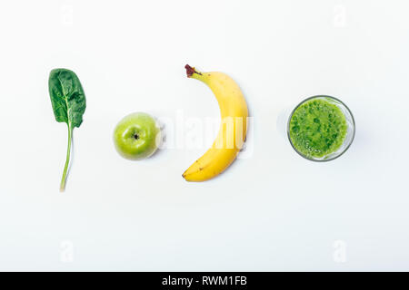 Blick von oben auf die ganzen Zutaten und Bereit-grünen Smoothie in Glas auf weißem Hintergrund gemacht, kopieren. Spinat Blatt, Apfel und Banane gemischt in einem heilen Stockfoto