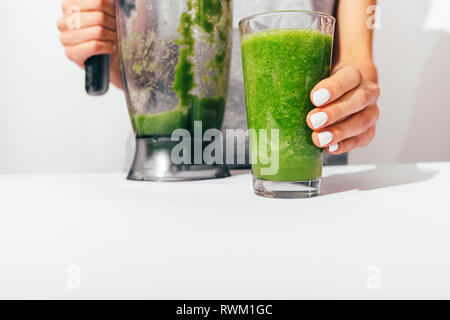 Die Frau Hände mit weißen Maniküre holding Blender und Glas frisch grün gemacht Smoothie am Küchentisch, close-up. Stockfoto