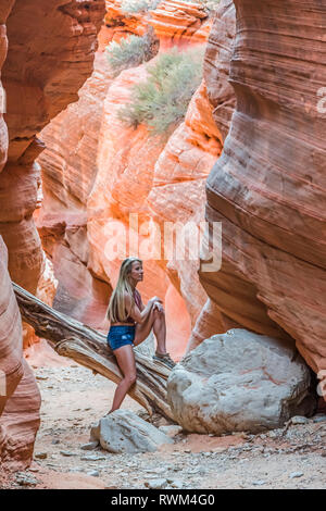 Eine Frau mit langen, blonden Haaren sitzt auf einem Anmelden Peek-A-Boo Gulch, ein Slot Canyon im Grand Staircase - Escalante Gebiet Stockfoto