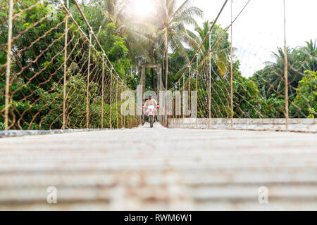 Motorradfahrer mit Surfbrett auf der Seilbrücke, Pagudpud, Ilocos Norte, Philippinen Stockfoto