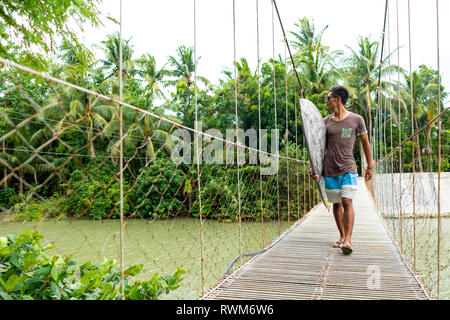 Mann mit Surfbrett auf der Seilbrücke, Pagudpud, Ilocos Norte, Philippinen Stockfoto