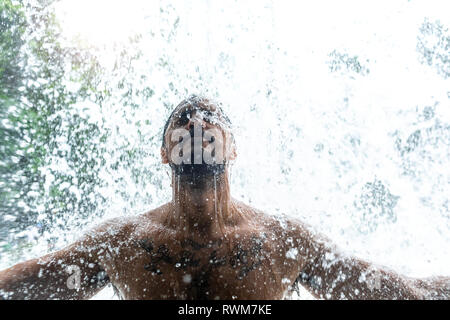 Mann unter erfrischenden Wasserfall Stockfoto