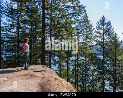 Eine Frau steht am Steinbruch Felsen auf dem Baden-Powell Trail mit Blick auf die Küstenlinie, Deep Cove, North Vancouver, Vancouver, British Columbia, Kanada Stockfoto