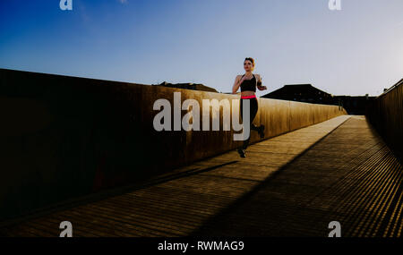 Junge Dame in Sportkleidung auf Wanderweg in sonniges Wetter mit blauem Himmel läuft Stockfoto