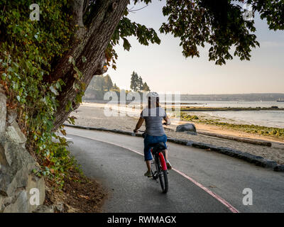 Eine Frau fährt Fahrrad entlang der Stanley Park Seawall Trail; Vancouver, British Columbia, Kanada Stockfoto