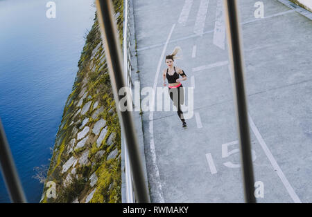 Von oben Blick durch Zaun von junge Dame in Sportswear läuft am Kai in der Nähe von Wasser in der Stadt Stockfoto