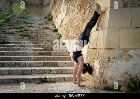 Frau macht Handstand gegen die Wand außerhalb Stockfoto