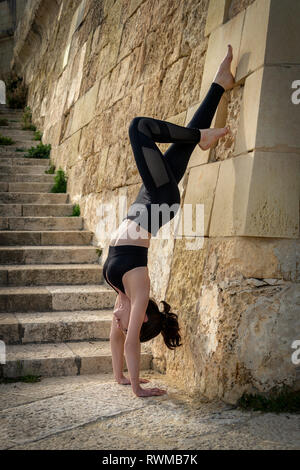 Frau macht Handstand gegen die Wand außerhalb Stockfoto