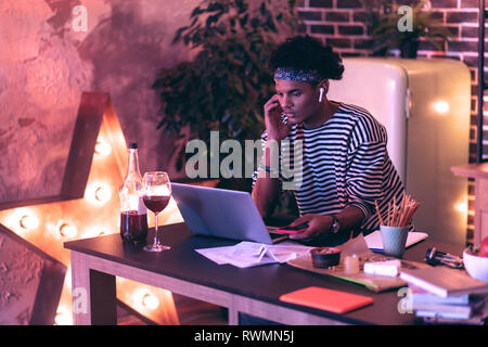 Kerl in einem gestreiften Pullover stehend an den Tisch neben dem Laptop, und schließen Sie es an das Telefon. Stockfoto