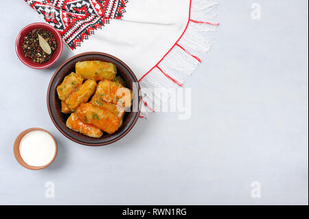 Gefüllte Kohlblätter mit Reis und Fleisch in Tomatensauce auf einem Handtuch bestickt auf grauem Hintergrund. Serviert mit Pfeffer und Sauerrahm. Stockfoto