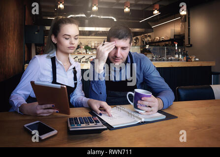 Junge Unternehmer über Dokumente im Restaurant. Auf tisch Telefon, Tablet, Tasse Kaffee, Notebook Stockfoto