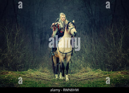 Kriegerin auf einem Pferd im Wald. wunderschönen skandinavischen Viking Reiten mit Axt in der Hand, blonde Haare in traditioneller Kleidung mit Fell colla Stockfoto