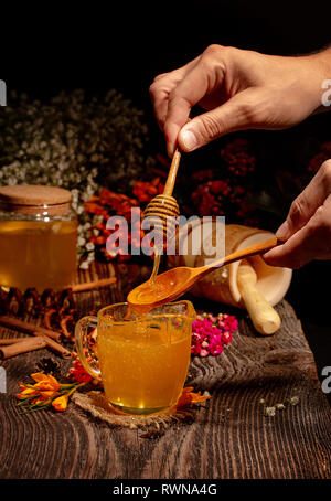 Honig Glas mit einem Löffel für Honig in den Händen. Rustikale Tabelle Stockfoto