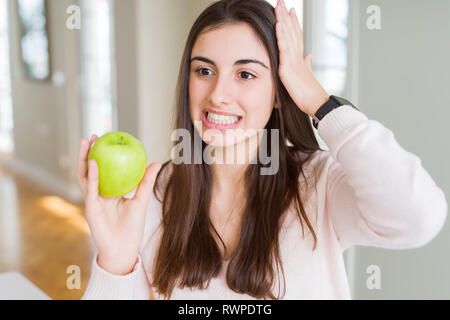 Schöne junge Frau das Essen gesund grüner Apfel Frucht mit Hand betonte am Kopf, mit Scham und Überraschung Gesicht schockiert, wütend und frustriert. Angst ein Stockfoto