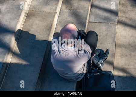 Aus der Vogelperspektive slim älterer Mann mit schütterem Haar grau, sitzen auf den Schritt in die Sonne Stockfoto