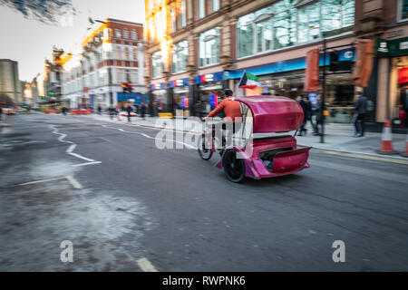 Rikscha Fahrer auf seinem violetten taxi Trike, durch die Straßen von London bewegen Stockfoto