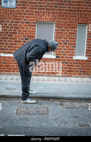 Obdachlose, die London Street ältere Menschen bücken suchen die Straße Rinne für verwendet und entsorgte Zigarettenkippen Stockfoto