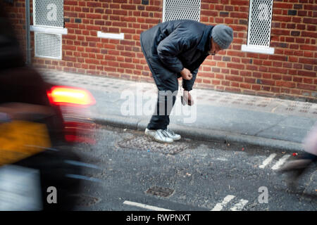 Obdachlose, die London Street ältere Menschen bücken suchen die Straße Rinne für verwendet und entsorgte Zigarettenkippen Stockfoto