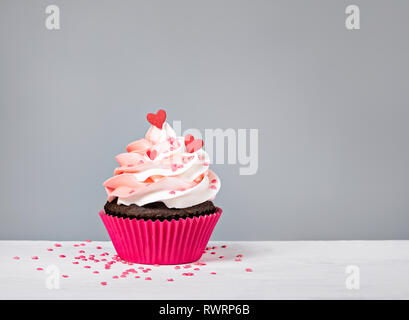 Valentines Tag Cupcake behandeln mit buttercream Vereisung und Herzen besprengt auf grauem Hintergrund Stockfoto