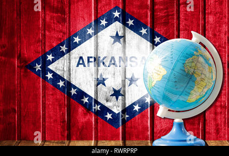 Globus mit einer Weltkarte auf einem hölzernen Hintergrund mit dem Bild des Flaggenstaates von Arkansas. Das Konzept der Reisen und Freizeit im Ausland. Stockfoto