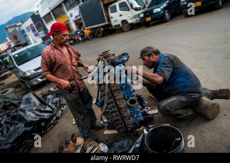 Kolumbianische Automechaniker arbeiten an einem LKW-Motor vor einer Autowerkstatt im Barrio Triste, Medellín, Kolumbien. Stockfoto