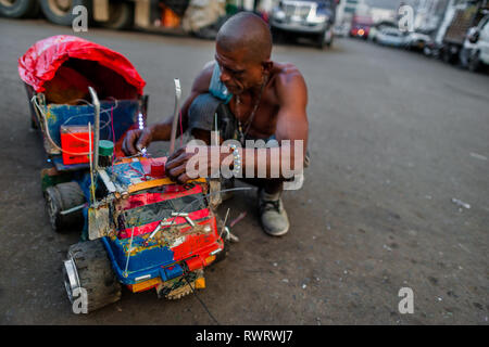 Ein kolumbianischer Mensch behebt einen hausgemachten Lkw Spielzeug Modell auf der Straße von Barrio Triste, einem Automechaniker Nachbarschaft in Medellín, Kolumbien. Stockfoto