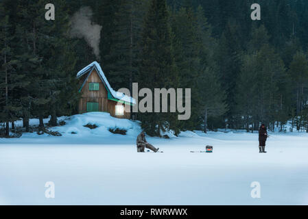 Shiroka poliana Dam, Bulgarien. 03,02,2019: Kleines Holzhaus in den Berg. Gefrorenen See vor mit Schnee bedeckt. Eis fishermans vor. Stockfoto