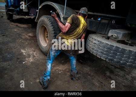 Eine kolumbianische Automechaniker arbeitet mit Brecheisen auf Suspension System eines Fahrzeugs in einer Autowerkstatt im Barrio Triste, Medellín, Kolumbien. Stockfoto