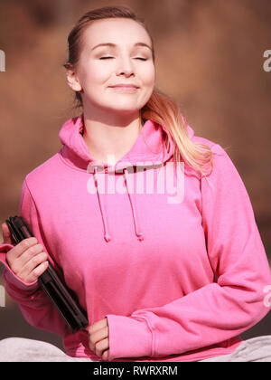 Fitness junge Frau sport Jugendmädchen mit engen Augen in Pink tracksuit Holding tablet Touchpad Computer erhalten die Sonne auf ihr Gesicht outdoor. Feder Stockfoto