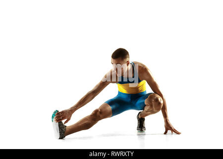 Jungen kaukasischen Mann Aufwärmen vor dem Laufen auf weiße studio Hintergrund isoliert. Eine männliche Läufer oder Jogger. Silhouette von Stretching Athlet mit Schatten. Stockfoto