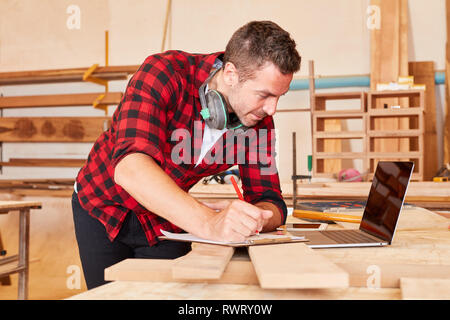 Handwerker mit Zwischenablage in der Werkstatt am Laptop in der Planung befinden. Stockfoto