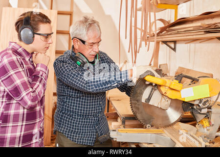 Handwerker master Trainee erklärt die Arbeit an die Säge in der Zimmerei chop Stockfoto