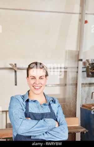 Stolz darauf, junge Frau als Handwerker Auszubildende mit verschränkten Armen in der Werkstatt Stockfoto