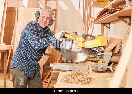 Alte Handwerker master mit Gehörschutz bei der Chop sah in seiner Tischlerei Stockfoto