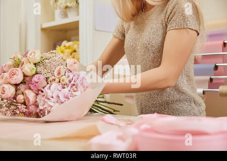 Croppedl Ansicht der Florist umhüllen Blumenstrauß aus Rosen und Pfingstrosen am Arbeitsplatz Stockfoto