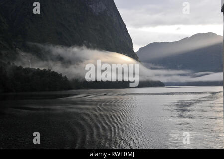 Um Neuseeland - die Sonne klettern über die umliegenden Berge und das Fangen einer Wolke über Doubtful Sound, Stockfoto