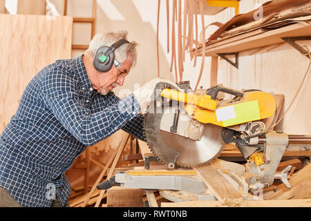 Ältere Menschen als Handwerker mit Erfahrung an der Säge in seiner Tischlerei chop Stockfoto