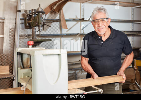 Senior als Schreiner oder Tischler arbeitet mit einem Strahl auf der Hobelmaschine Stockfoto