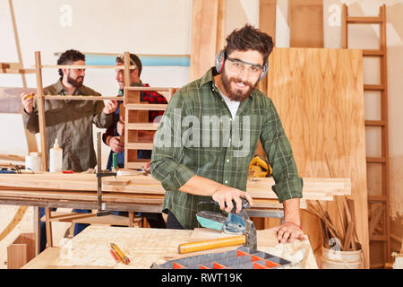 Junger Mann als Tischler Lehrling arbeitet mit der Schleifmaschine in der Schreinerei Stockfoto