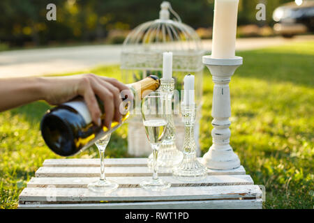 Frau giesst Sekt aus der Flasche mit Glas an sonnigen, grünen Park. Stockfoto