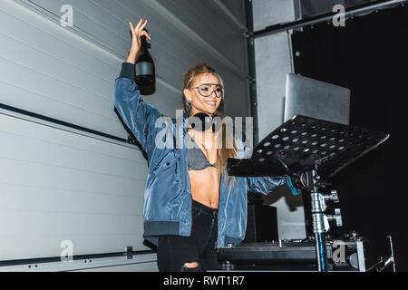 Happy dj-Frau mit Flasche mit Wein in der Hand, während Sie mit Laptop Stockfoto