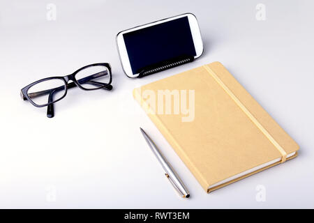 Modernes weißes Büro Schreibtisch Tisch mit Laptops, Smartphones und andere Verbrauchsmaterialien. Leere Seite "Notizbuch für die Eingabe der Text in der Mitte. Ansicht von oben. Stockfoto