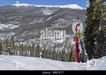Notrufzeichen und Geschwindigkeitskontrollschild auf einem schneebedeckten Berghang in einem Skiresort in Colorado, USA, mit den Rocky Mountains im Hintergrund Stockfoto