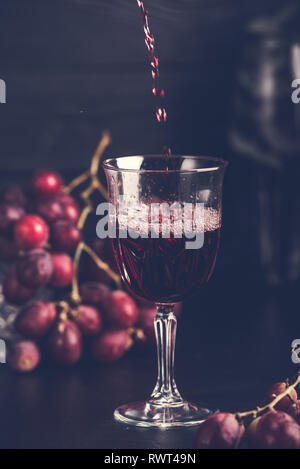 Lila Trauben mit Traubensaft in einem Glas, dunkles Bild. Stockfoto