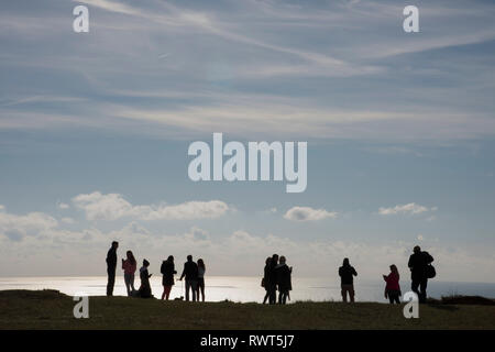 Gemischte Gruppe von Menschen in Silhouette stehen am Rand von Beachy Head auf der South Downs Way England UK. Stockfoto