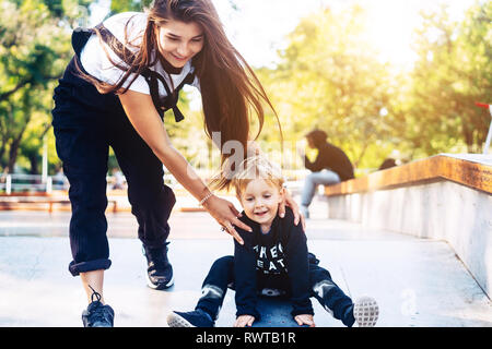 Junge Mutter lehrt, ihren kleinen Jungen ein Skateboard zu fahren Stockfoto