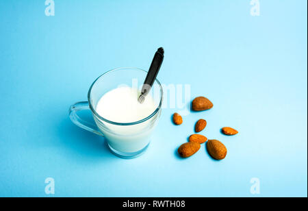 Mandelmilch und Nüsse in ein Glas vor blauem Hintergrund Stockfoto