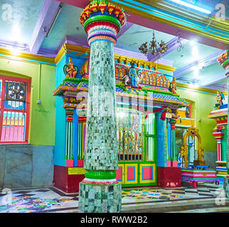 YANGON, MYANMAR - 15. FEBRUAR 2018: Die malerische Stein Spalte in Sri Varatha Raja Perumal Temple mit bunten relief Kapital und kleinen Schrein in Templ Stockfoto