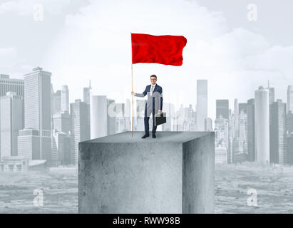 Gut aussehender Geschäftsmann auf der Oberseite der Stadt mit Red Flag Stockfoto